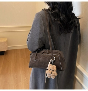 Detail of dark brown suede underarm bag with white stitching and plush bear charm