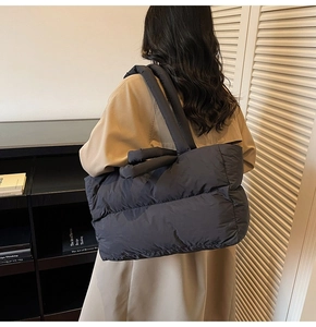 Detailed view of black quilted down tote bag with padded handles on a model's shoulder
