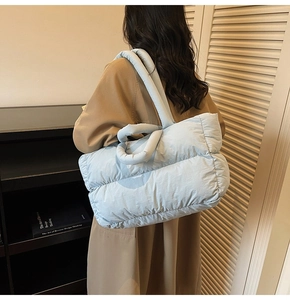 Light blue quilted puffer tote bag shown on model with shoulder strap and thick handle