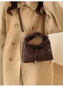 Close-up of dark coffee crossbody bag with a slim bow detail on a beige coat outfit