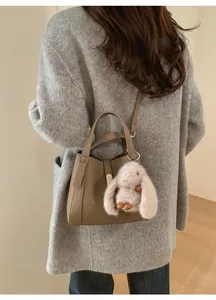Khaki leather handbag with rabbit plush charm worn by model in grey faux fur coat