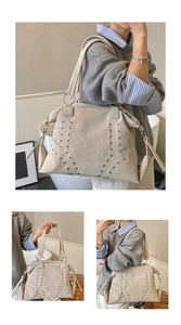 Detail view of large beige tote bag with metallic rivet patterns and smooth zipper