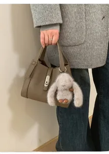 Close-up of brown pebbled leather handbag with silver buckle and plush rabbit charm