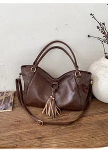 Detail of vintage brown leather tote bag featuring woven stitching and tassel accents