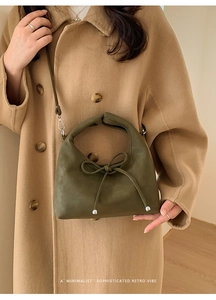 Olive green suede crossbody bag with bow detail shown on model in minimalist setting