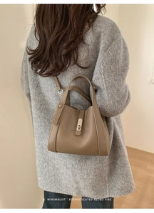 Detail of a brown leather bucket bag with silver clasp worn with a grey sweater