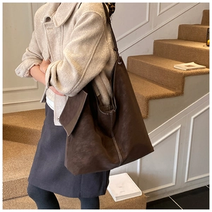 Macro detail of large brown tote bag with white contrast stitching on matte leather surface