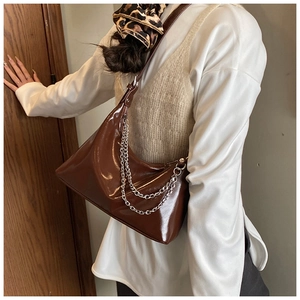 Détail d'un sac d'épaule en cuir verni marron avec chaînes argentées porté par un modèle