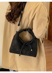 Close-up of a black suede handbag with a unique knot detail on a beige trench coat