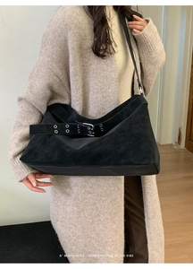 Detail of black suede tote bag with silver buckle strap worn with a beige sweater