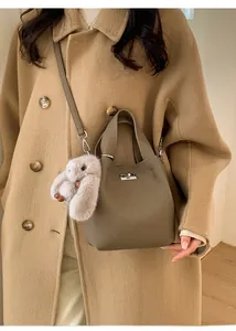 Close-up of taupe bucket bag with leather texture, metal lock, and plush bunny charm
