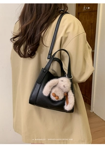 Detail of black pebbled leather bucket bag with cute plush rabbit charm on a model