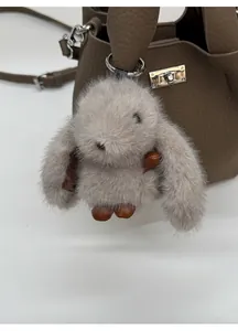 Detail of grey plush rabbit pendant with silver metal ring on a brown leather bucket bag