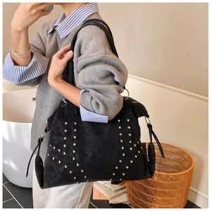 Detail of black suede tote bag with silver rivets and wide handle in a home setting
