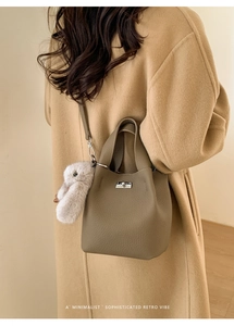 Detail of a brown lychee pattern bucket bag with a silver twist lock and plush bunny charm