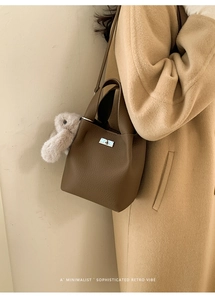 Brown lychee leather bucket bag with silver clasp and plush rabbit charm on a wool coat