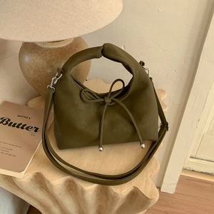 Detail of olive green handbag with bow drawstring and silver hardware on wooden table