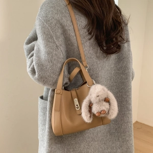 Close-up of light brown lychee grain leather bucket bag with silver lock and plush bunny charm