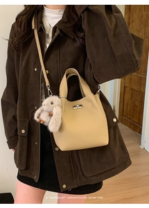 Detail of a beige leather bucket bag with a metal turn-lock and a grey plush bunny charm