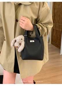 Close-up of black leather bucket bag with silver rotating lock and plush rabbit charm