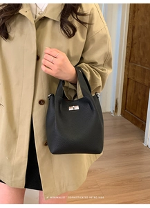Close-up of black pebble leather bucket bag with silver hardware on a beige trench coat
