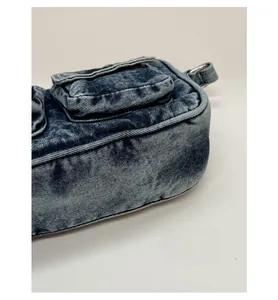 Close-up of washed blue denim shoulder bag featuring reinforced bottom and side metal ring