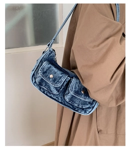 Detail of blue washed denim shoulder bag with vintage utility pockets and metal buckles