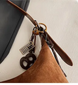 Dettaglio di una borsa a tracolla in pelle scamosciata marrone con ciondolo abaco e pretzel