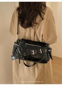Detail of black faux leather crossbody bag with silver zippers and wide eyelet strap