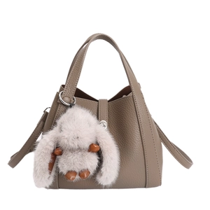 Taupe pebbled leather bucket bag with top handle and plush rabbit charm on white background