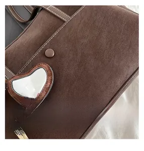 Detail of dark brown leather bag showing white contrast stitching and heart mirror charm