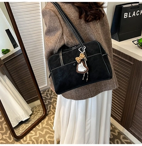 Detail of black suede shoulder bag with contrast stitching and leopard print bow charm
