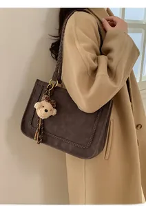 Detail of dark brown tote bag with woven texture and bear charm worn on beige coat