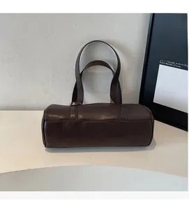 Detail of a dark brown oiled leather barrel bag on a minimalist display stand