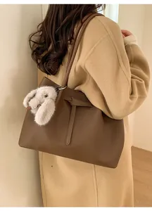 Detail of dark brown leather tote bag with pebble texture and cute plush rabbit charm