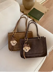 Detail of frosted suede tote bags with woven rope handles and cute bear charms on a sofa