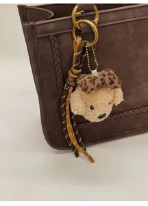 Close-up of plush dog charm with leopard bow on retro shoulder bag strap