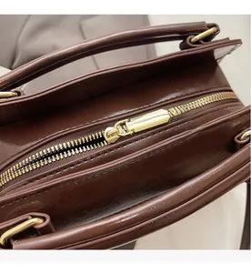 Détail du sac à main marron foncé montrant la fermeture dorée et le cuir lisse