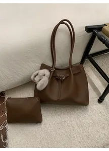 Deep brown textured leather tote bag set with plush bunny pendant on cozy white bedding