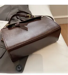 Détail d'un sac bandoulière marron en cuir avec nœud latéral et boucles dorées chic