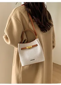 Detail of a white woven bucket bag with brown leather trim worn by a model in a camel coat
