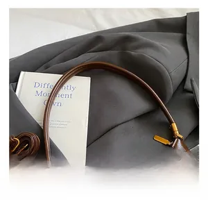 Détail d'un sac demi-lune en cuir ciré marron avec finitions dorées et bandoulière
