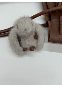 Detail of a fluffy grey plush rabbit keychain with brown leather accents on a tote bag