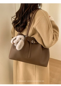Brown leather tote bag featuring a cute beige plush bunny pendant and a buckle strap detail