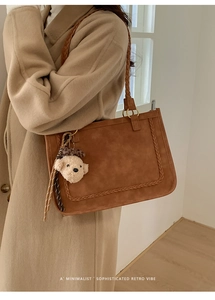 Detail of a brown suede tote bag featuring braided strap handles and a plush bear charm