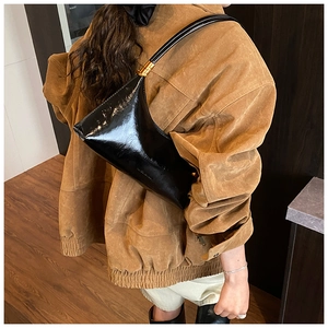 Détail d'un sac sous le bras en cuir noir brillant avec anneaux dorés sur un mannequin