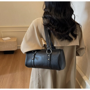 Détail du sac polochon en cuir noir avec ferrures argentées porté à l'épaule