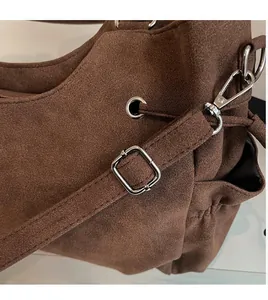 Detalle de la correa ajustable con hebilla plateada en el bolso de ante marrón