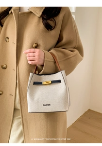Detail of canvas bucket bag with leather handle and golden metal twist lock closure