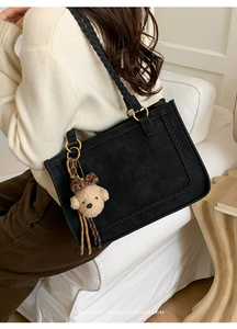 Close-up of black suede tote bag with woven edges and leopard print bear charm